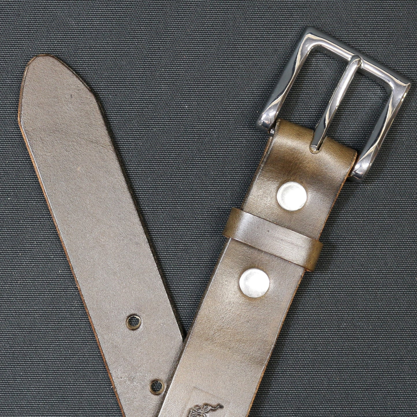 A brown leather belt with nickel buckle and rivets.